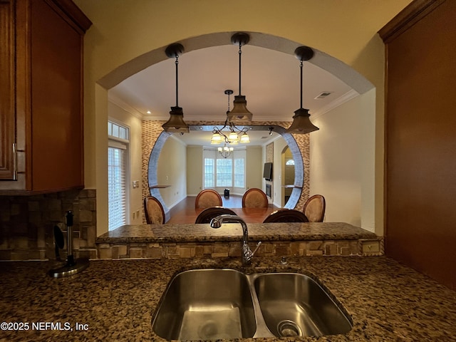 details with dark stone countertops, a sink, decorative light fixtures, and crown molding