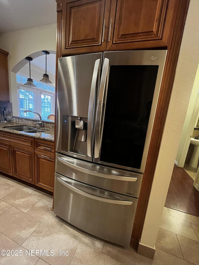 kitchen featuring arched walkways, a sink, stainless steel refrigerator with ice dispenser, dark stone counters, and decorative light fixtures