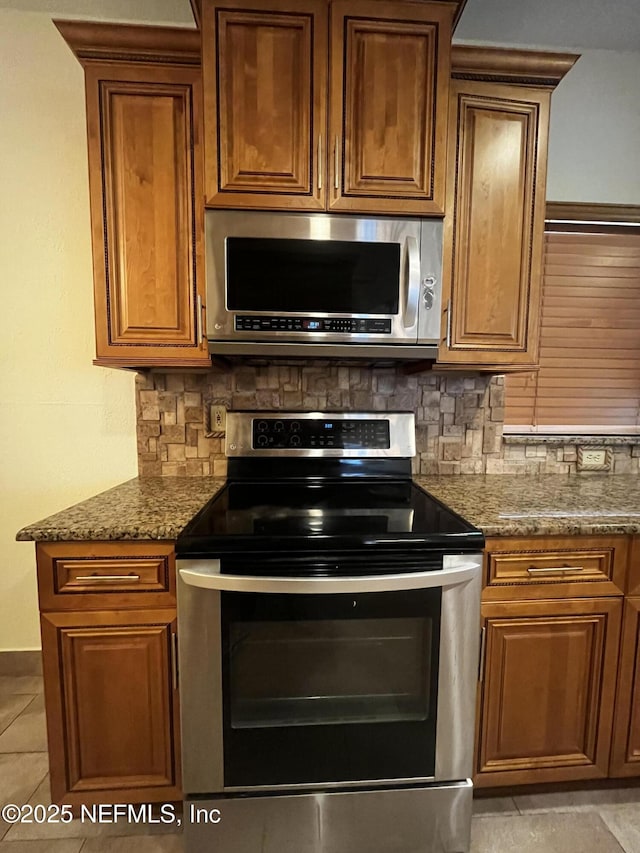 kitchen featuring stainless steel appliances, brown cabinetry, dark stone countertops, and decorative backsplash