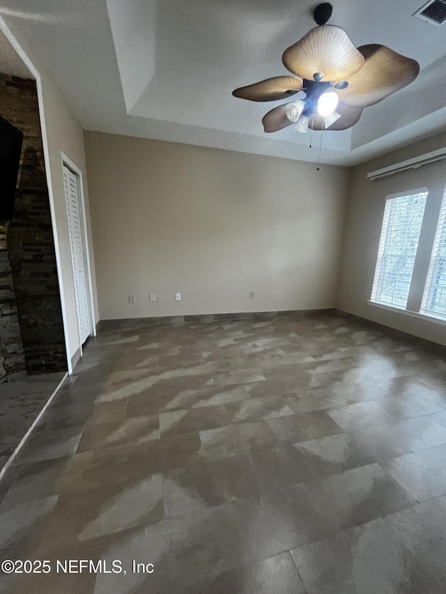 spare room with a ceiling fan, a raised ceiling, visible vents, and baseboards