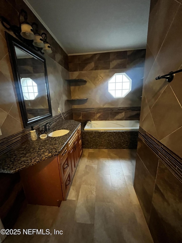 full bathroom featuring tasteful backsplash, ornamental molding, vanity, tiled tub, and tile walls