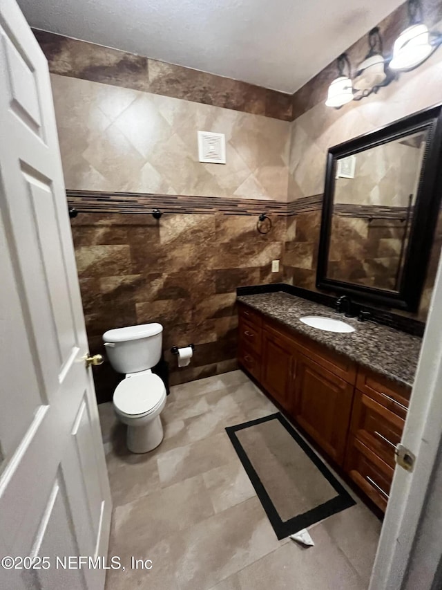 bathroom with tile walls, toilet, and vanity