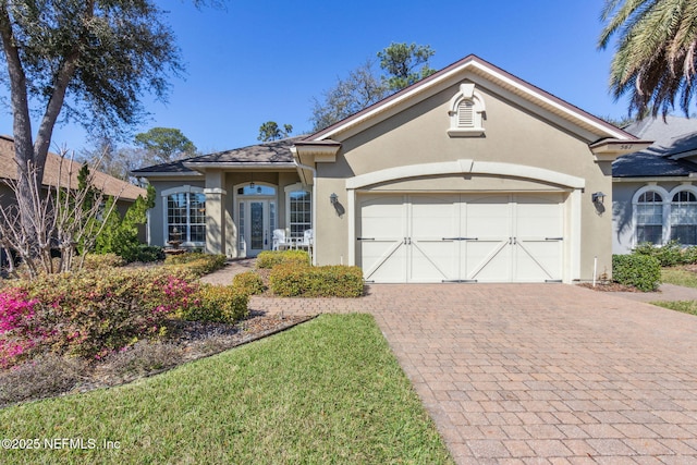 ranch-style home featuring french doors, decorative driveway, an attached garage, and stucco siding