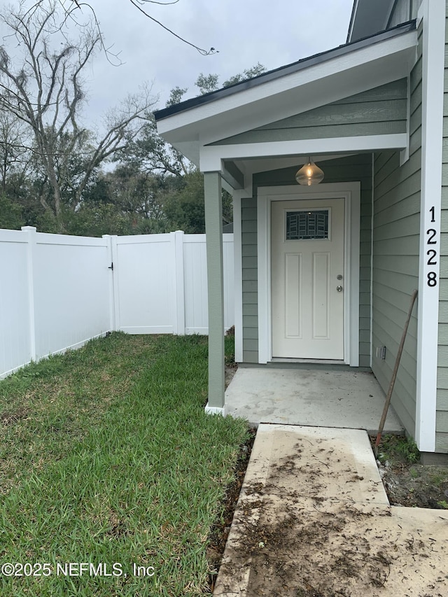 view of exterior entry featuring a lawn and fence