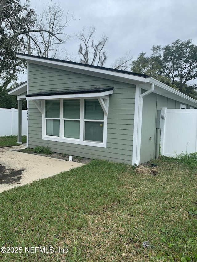 view of property exterior featuring fence, driveway, and a lawn