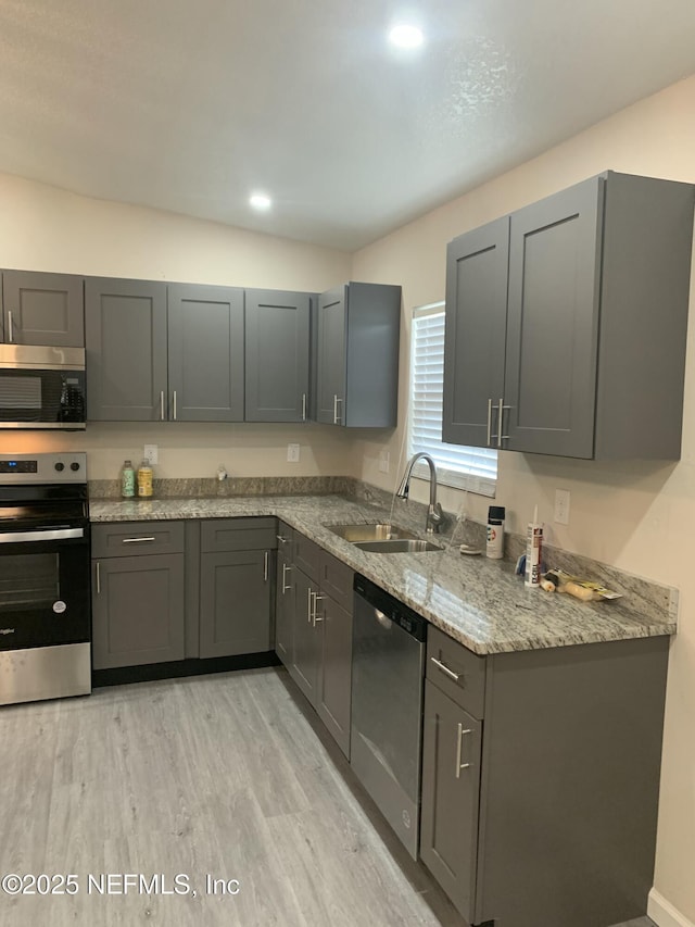 kitchen featuring light wood finished floors, light stone counters, stainless steel appliances, gray cabinetry, and a sink