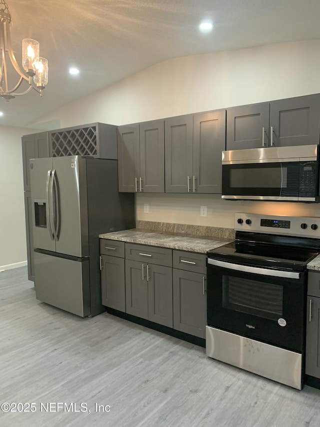 kitchen featuring stainless steel appliances, lofted ceiling, light countertops, light wood-style flooring, and an inviting chandelier