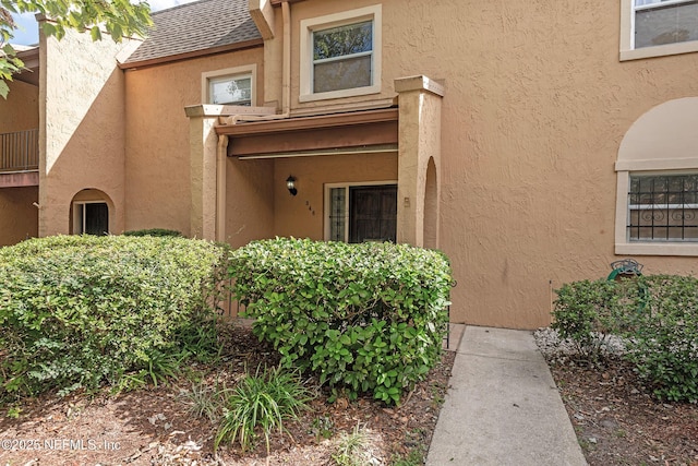 entrance to property featuring stucco siding and roof with shingles