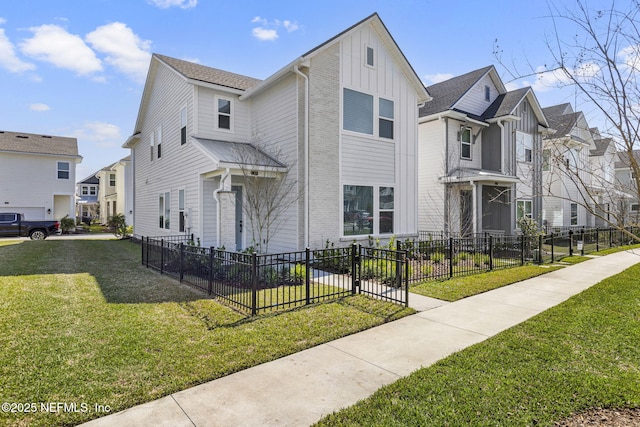 view of front of house with board and batten siding, a front yard, brick siding, and a fenced front yard