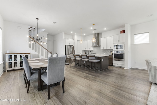 dining area with recessed lighting, stairway, an inviting chandelier, light wood-style floors, and baseboards