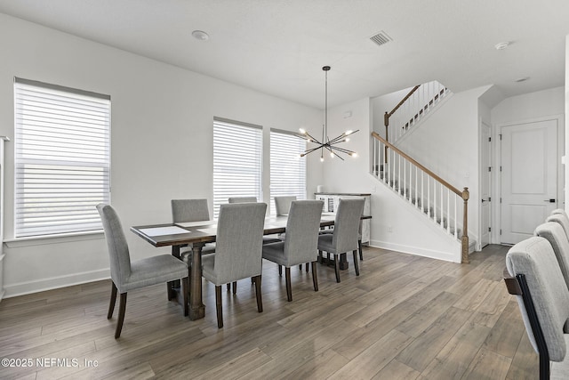 dining room featuring a notable chandelier, wood finished floors, visible vents, stairway, and a wealth of natural light