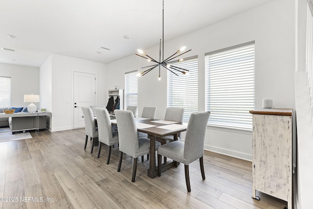 dining space with a healthy amount of sunlight, light wood-style floors, baseboards, and a notable chandelier