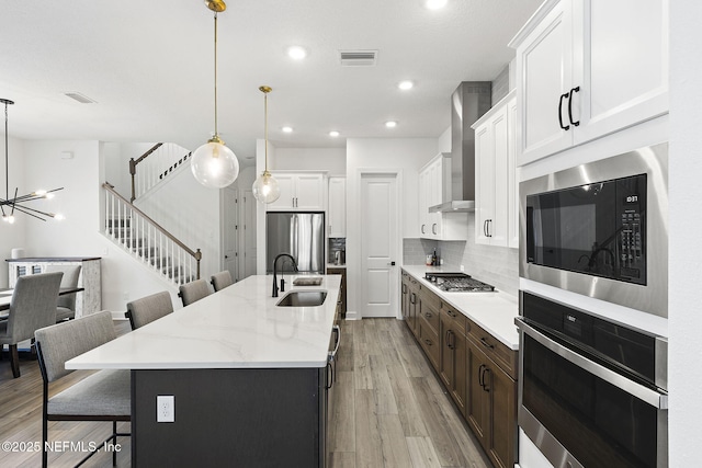 kitchen featuring a breakfast bar area, stainless steel appliances, a sink, visible vents, and wall chimney exhaust hood