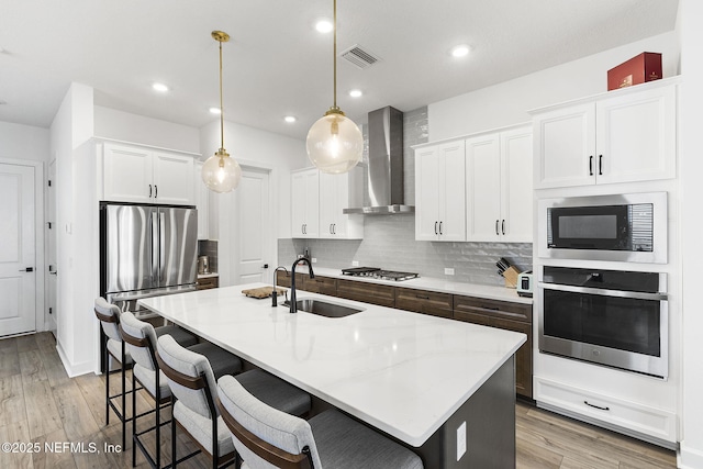 kitchen with visible vents, decorative backsplash, appliances with stainless steel finishes, a sink, and wall chimney range hood