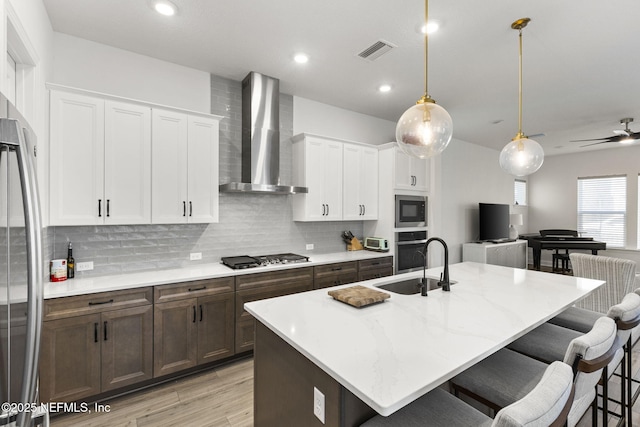 kitchen with visible vents, appliances with stainless steel finishes, a kitchen breakfast bar, wall chimney range hood, and a sink