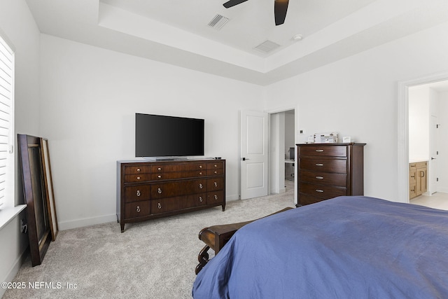 bedroom featuring a raised ceiling, light colored carpet, visible vents, ensuite bathroom, and baseboards