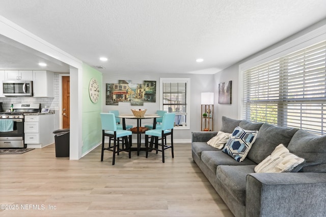 living room with a textured ceiling, light wood-style flooring, recessed lighting, visible vents, and baseboards