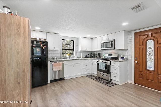 kitchen with white cabinetry, visible vents, light wood-style floors, appliances with stainless steel finishes, and decorative backsplash