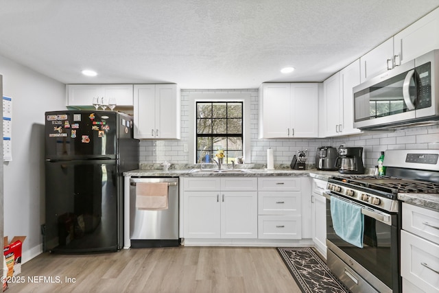 kitchen featuring backsplash, appliances with stainless steel finishes, white cabinetry, a sink, and light wood-type flooring