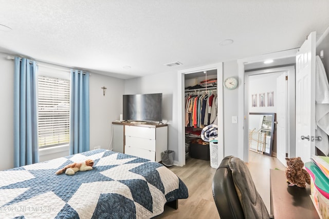 bedroom featuring light wood-type flooring, a closet, visible vents, and a textured ceiling