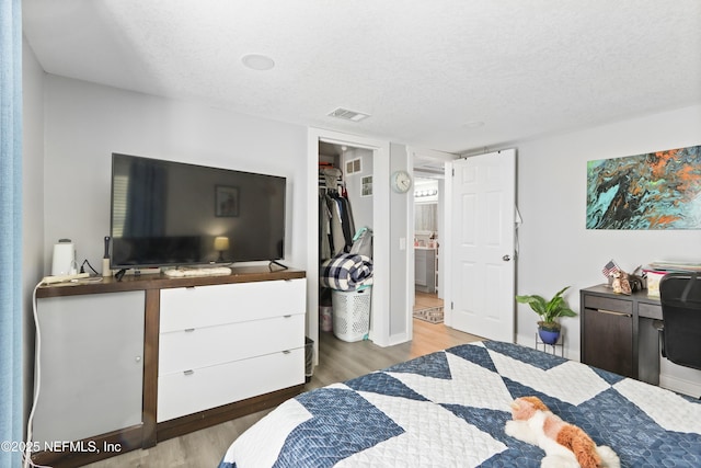 bedroom with a spacious closet, visible vents, a textured ceiling, and wood finished floors