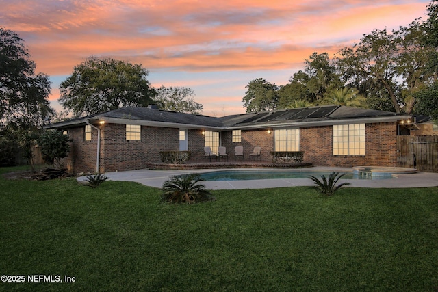 back of house at dusk featuring a patio, a yard, brick siding, and an outdoor pool