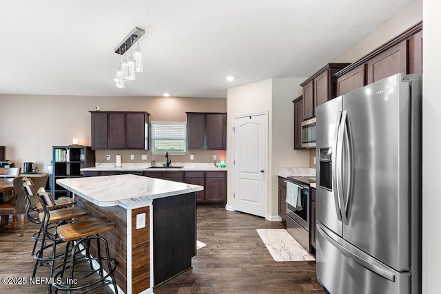 kitchen featuring stainless steel appliances, a sink, dark brown cabinets, light countertops, and dark wood-style floors