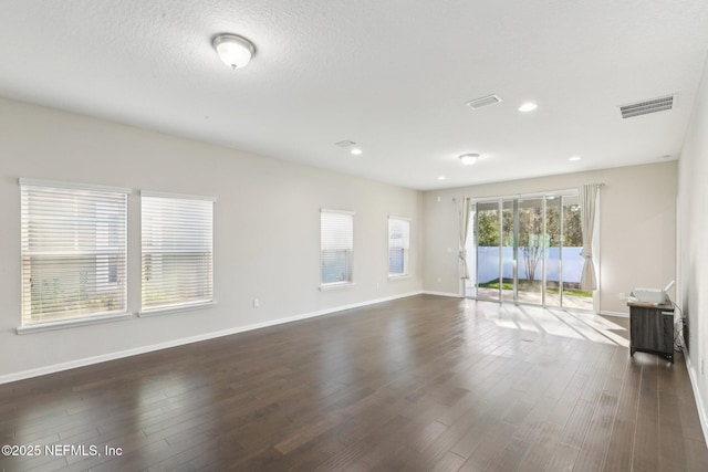 unfurnished living room with a textured ceiling, dark wood finished floors, visible vents, and baseboards