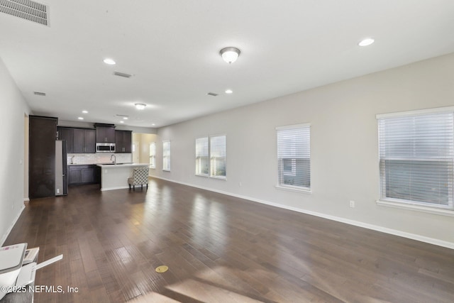 unfurnished living room featuring dark wood-style flooring, visible vents, and baseboards