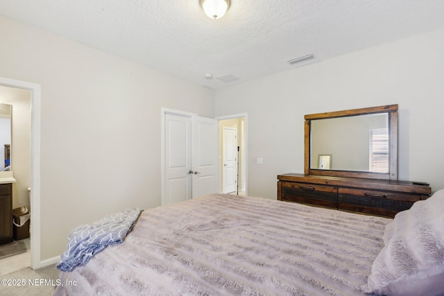 bedroom featuring a textured ceiling, carpet, ensuite bath, and visible vents