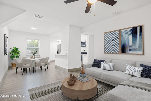 living area with ceiling fan, light wood-type flooring, visible vents, and baseboards