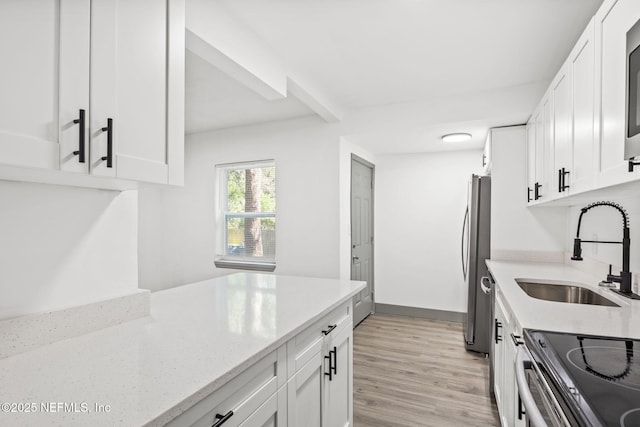 kitchen featuring white cabinets, light stone counters, stainless steel appliances, light wood-style floors, and a sink