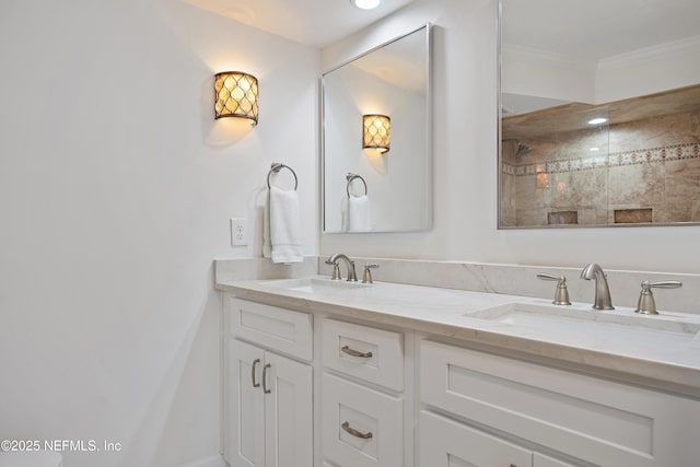 bathroom featuring a tile shower, double vanity, a sink, and crown molding