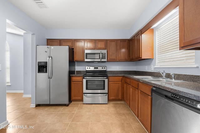 kitchen with light tile patterned floors, visible vents, appliances with stainless steel finishes, brown cabinetry, and a sink