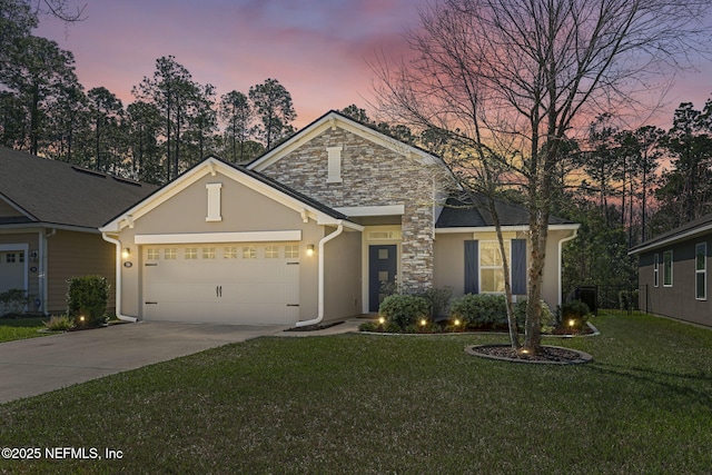 view of front of house featuring an attached garage, stone siding, driveway, a lawn, and stucco siding