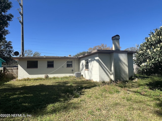 back of house featuring a yard, central AC unit, concrete block siding, and fence