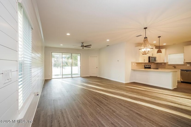 unfurnished living room with ceiling fan with notable chandelier, recessed lighting, baseboards, and wood finished floors