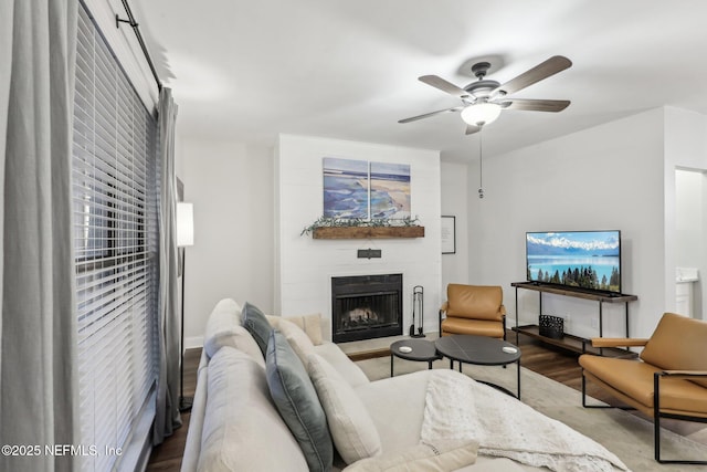 living room with a fireplace with raised hearth, a ceiling fan, and wood finished floors