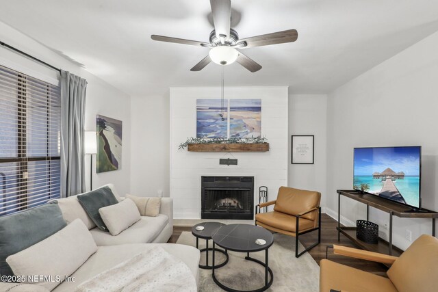 living area featuring ceiling fan, a fireplace, baseboards, and wood finished floors