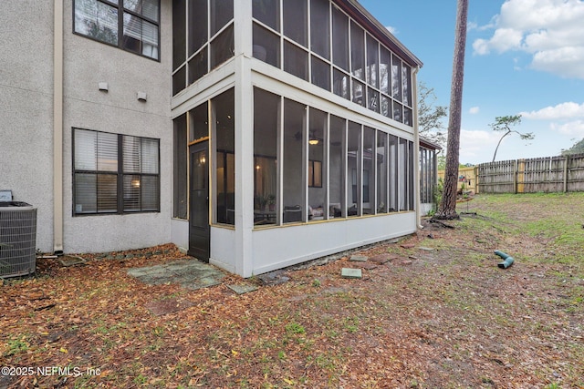 view of property exterior with cooling unit, a sunroom, fence, and stucco siding