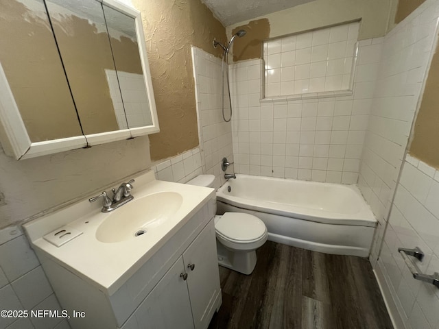 bathroom featuring a textured wall, toilet, tub / shower combination, vanity, and wood finished floors