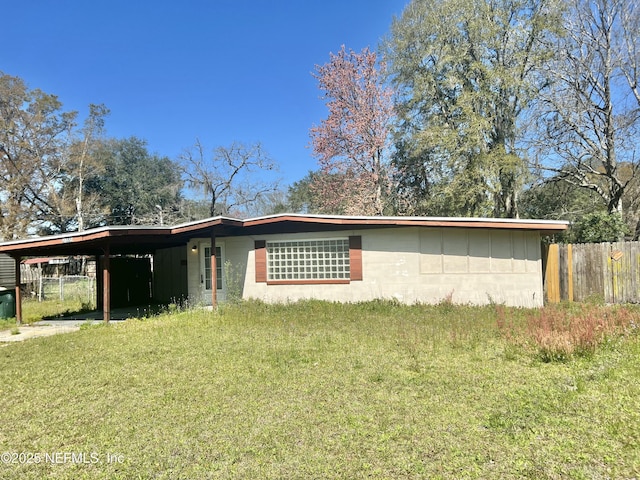 view of side of home featuring a carport, concrete block siding, fence, and a lawn