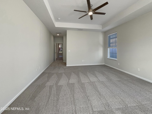 carpeted empty room with a raised ceiling, a ceiling fan, and baseboards