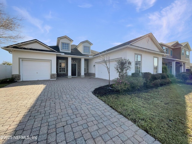 view of front of house featuring an attached garage, stone siding, decorative driveway, stucco siding, and a front lawn