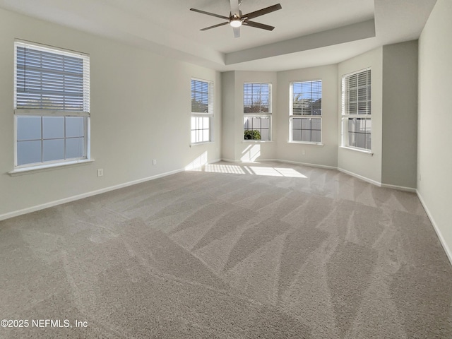 empty room with ceiling fan, a tray ceiling, carpet, and baseboards