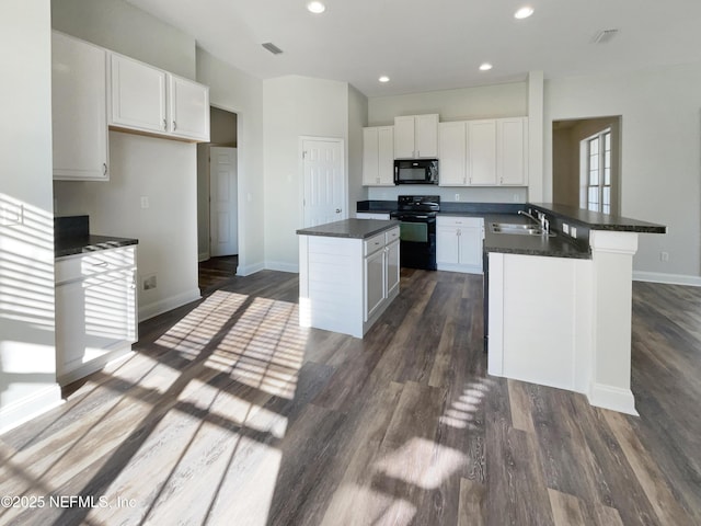 kitchen featuring a peninsula, a kitchen island, a sink, black appliances, and dark countertops