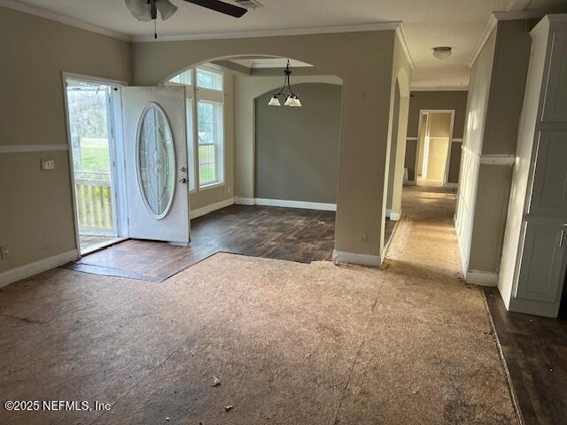 foyer entrance featuring ceiling fan with notable chandelier, baseboards, arched walkways, and ornamental molding