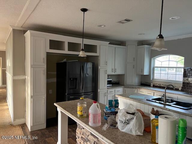 kitchen featuring visible vents, a sink, black fridge with ice dispenser, white cabinets, and crown molding