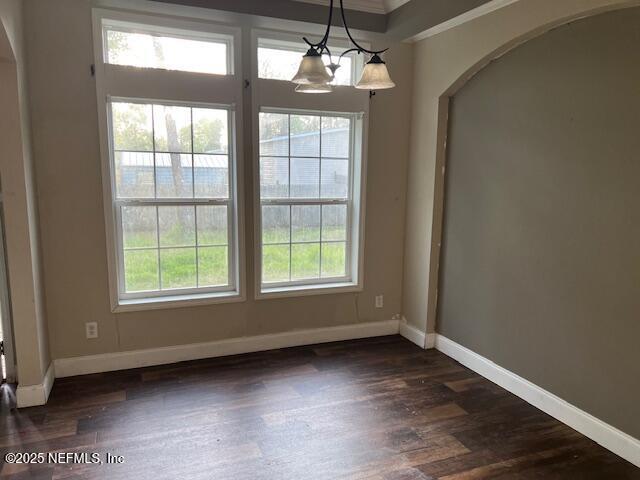 unfurnished dining area featuring baseboards, arched walkways, dark wood-style floors, and ornamental molding