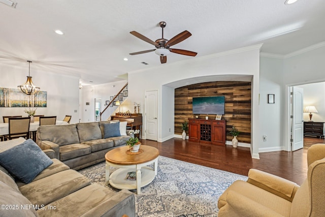 living room with stairway, wood finished floors, ornamental molding, and ceiling fan with notable chandelier